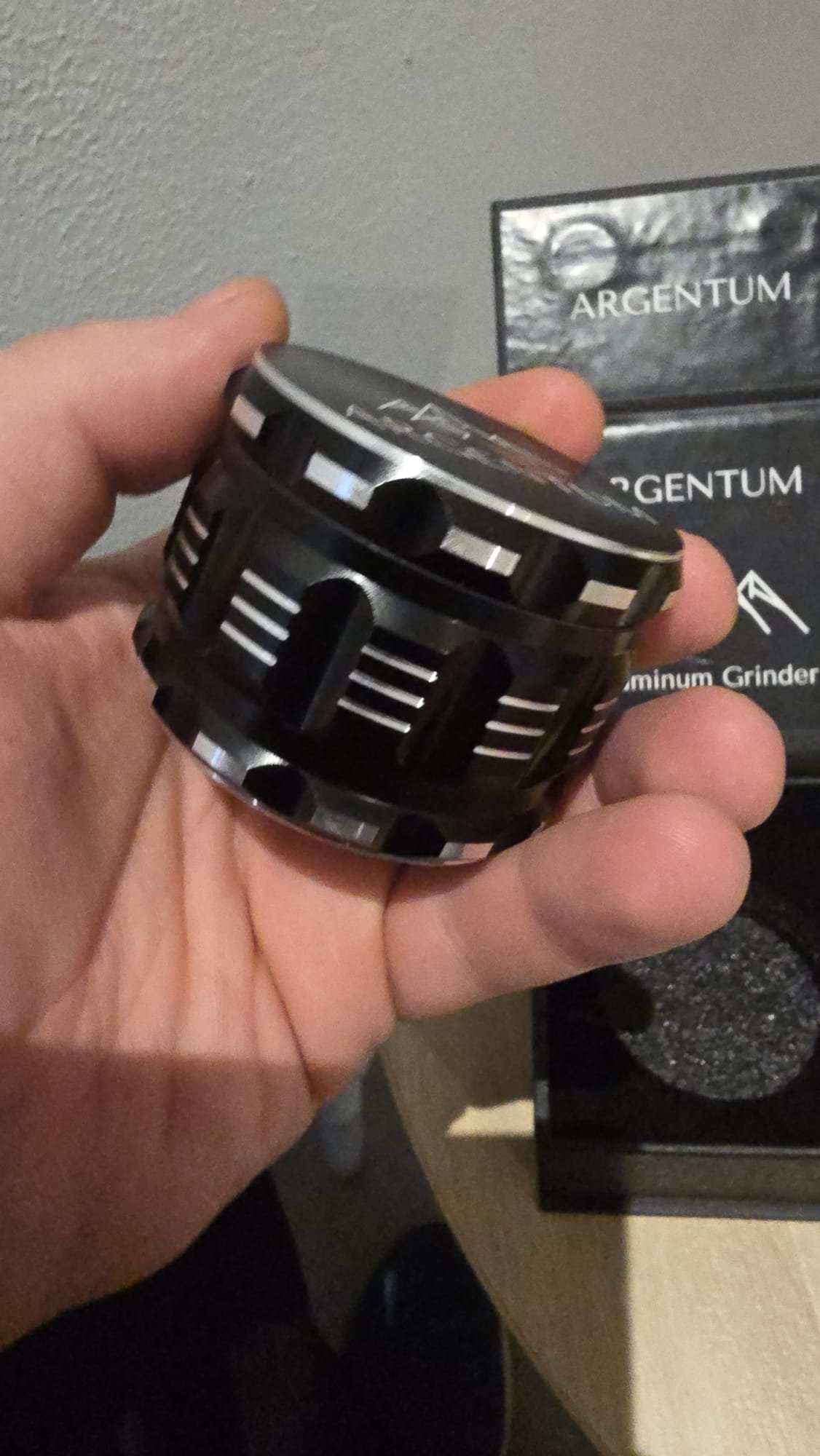 Hand holding the black ARGENTUM aluminum grinder, showing the milled grip ribs around the body
