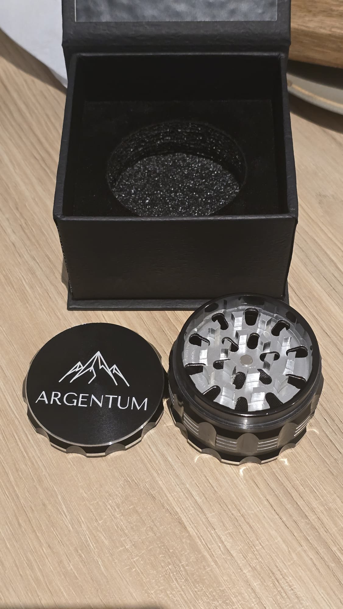 Open ARGENTUM grinder photographed from above showing the polished aluminum grinding teeth inside the top chamber